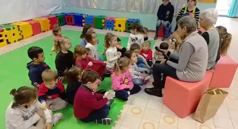 Bambini seduti in cerchio sul tappeto ascoltano una maestra
